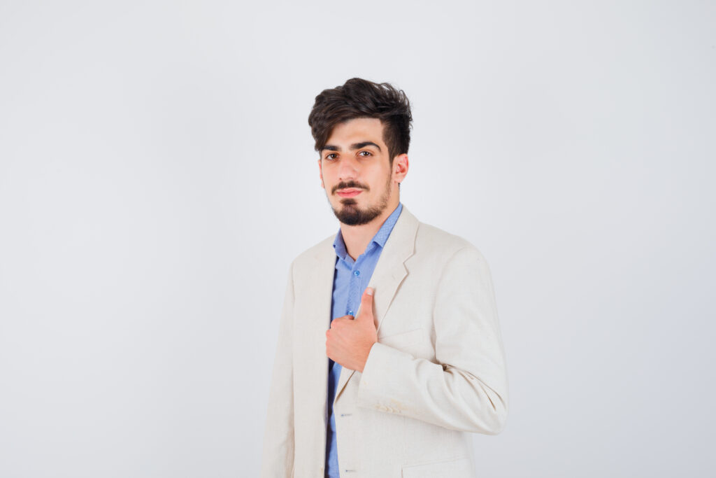 young boy showing thumb up in blue t-shirt and white suit jacket and looking serious , front view.